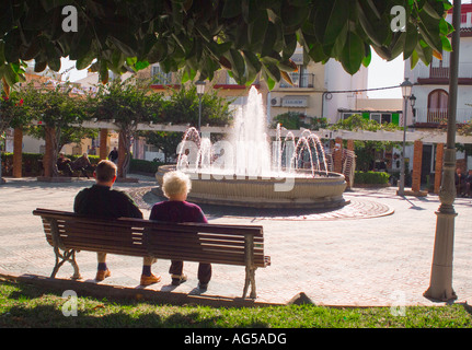 Elderly couple sitting on park bench watching fountain in Nerja Spain Stock Photo