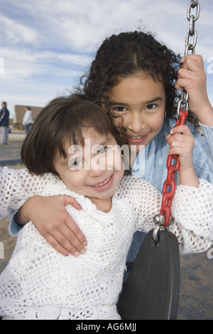 Hispanic sisters together on swing, outdoors, smiling Stock Photo