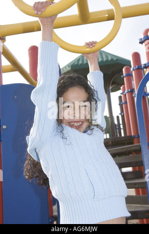 smiling ten year old hispanic girl hanging on monkey bars playground school age strength active healthy lifestyle education Stock Photo