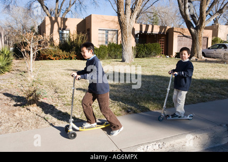 asian boys riding scooters on sidewalk, southwestern united states Stock Photo