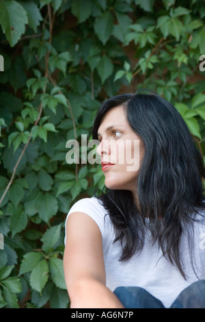 woman sitting outdoors thoughtful expression, green leaves, face profile Stock Photo