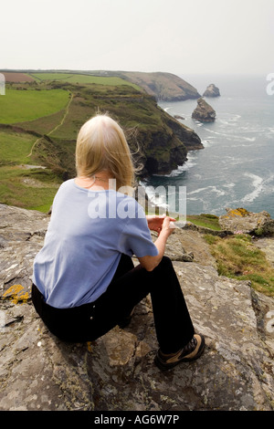 UK Cornwall Boscastle woman sat overlooking coastline west of Willapark Head Stock Photo