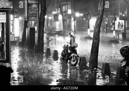 A scooter parked on a pavement on Boulevard Saint Michel in Paris during a rainstorm at night Stock Photo