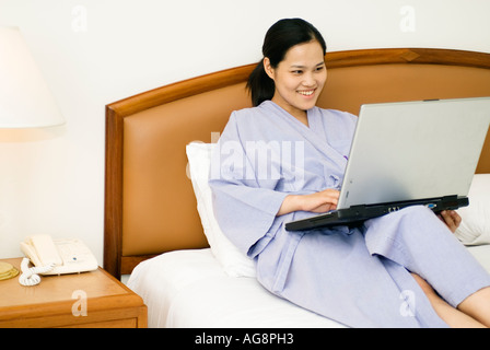 Chinese Young Woman Laying On Bed In Hotel Room Working On Laptop Computer Bangkok Thailand Stock Photo