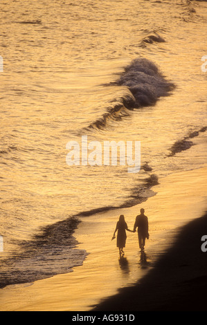 Couple walking along beach at waters edge at sunset Model released image Stock Photo