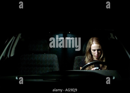 Caucasian Female Sat Alone In a Car Using a Mobile Cell Phone at Night Illuminated by the Cars Interior Light Stock Photo