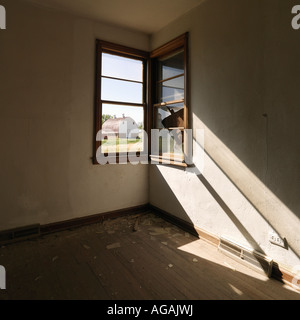 Dark empty abandoned room with sunrays stretching across wall from corner window Stock Photo