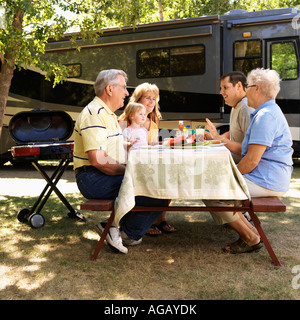 Three generation Caucasian family seated at picnic table in front of recreational vehicle talking Stock Photo