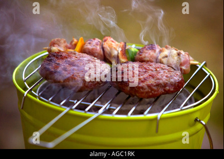 Beefburgers and kebab cook over a bucket-sized barbeque. Stock Photo