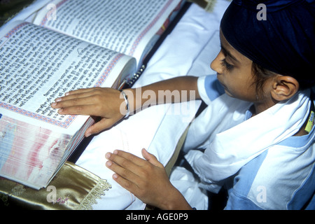 A young Sikh boy reading the Guru Granth Sahib, the Sikh holy book, in the gurdwara Stock Photo