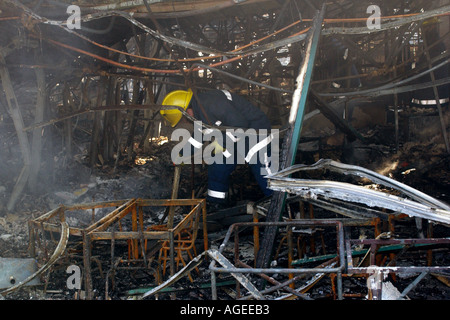 Firefighter sifting through the charred tangled remains of a classroom after a fire destroyed Rogerstone Primary School Stock Photo