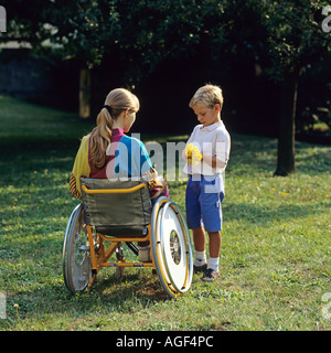 Little boy giving flowers to disabled woman in wheelchair in garden Stock Photo