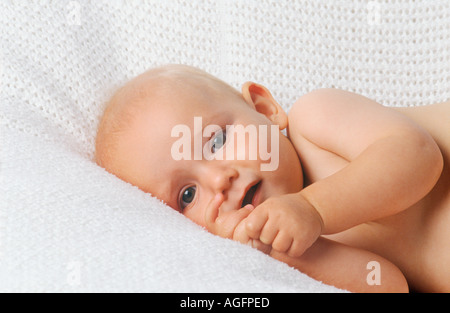 Portrait of 9 month old blonde baby boy lying quietly on white blanket sucking thumb Stock Photo