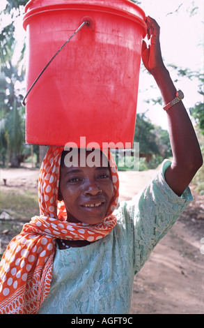 Local woman carrying water Wearing a colourful kanga on her head Chole island Mafia south of Zanzibar Tanzania East Africa Stock Photo