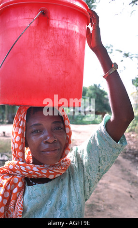 Local woman carrying water Wearing a colourful kanga on her head Chole island Mafia south of Zanzibar Tanzania East Africa Stock Photo