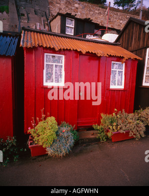 A shack dwelling red with flower troughs outside and with a wall in the backround The house has a roof made from tin Stock Photo