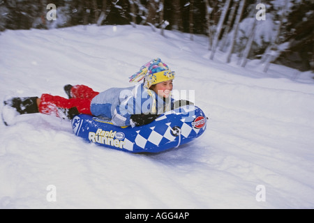 Young girl w big smile on face sliding down hill on innertube Girdwood Southcentral Alaska Winter Stock Photo