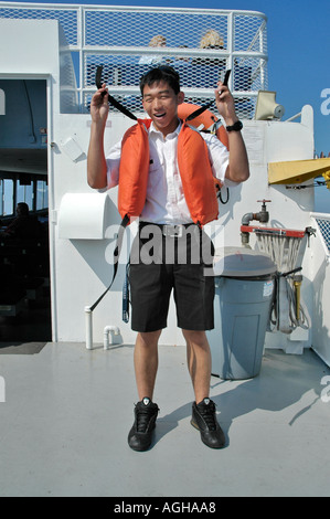 Asian American male demonstrates the proper use of a life vest on a boat tour on Lake Superior Michigan Upper Peninsula Stock Photo