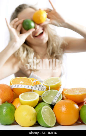 Woman holding orange and lime on eyes focus on fruits wrapped with measuring tape Stock Photo