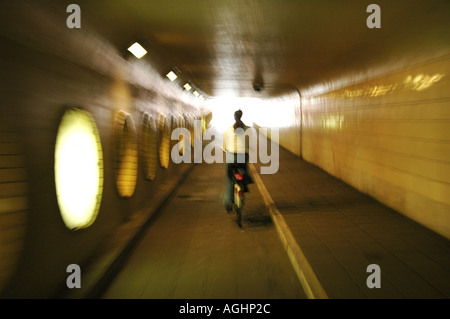 young woman cycling through dark tunnel alone Stock Photo