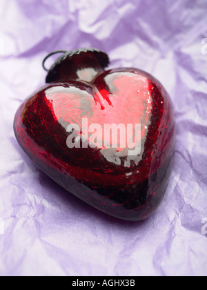 red heart shaped glass ornament laying on purple paper Stock Photo