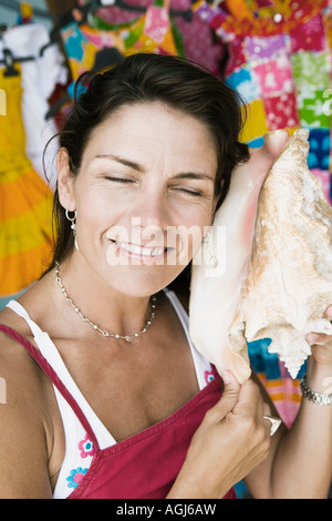 Close-up of a mid adult woman listening to a conch shell and smiling Stock Photo
