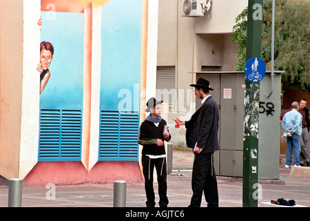 two religious Jews talking in the street with a woman graffiti looking at them Stock Photo