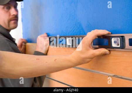 Two men working together to hang slat boards on blue wall using a level tool. Stock Photo