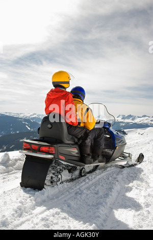 Man and woman riding on snowmobile in snowy mountainous terrain Stock Photo