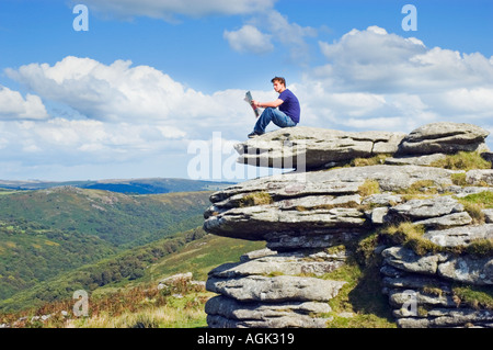 Young man sitting on a rock reading a magazine in open countryside Stock Photo
