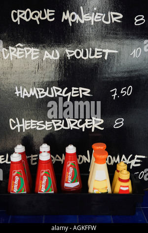 Close-up of tomato ketchup bottles in front of menu list on a blackboard Stock Photo