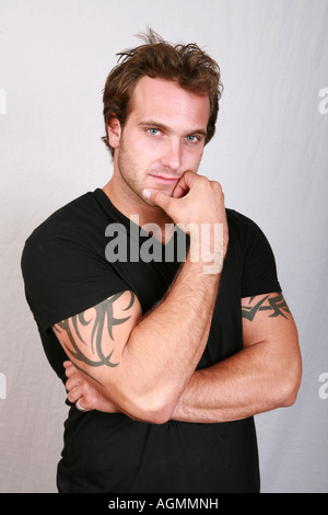 Attractive muscular 20's male with arm tattoos body art looking serious studious with crossed folded arms and hand on chin Stock Photo
