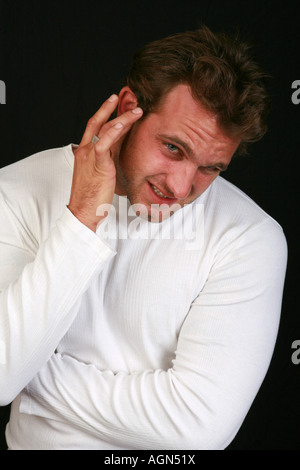Young 20s male man rubs ear with finger and hand suffering from pain and discomfort with severe chronic ear ache earache Stock Photo