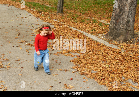 cute little girl walking in the woods forest leaves cute little girl wearing jeans and red shirt view from the top autumn leaves Stock Photo
