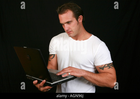 Young 20s male uses a laptop notebook computer PC with wireless Internet connection wearing white t shirt standing surfing Stock Photo