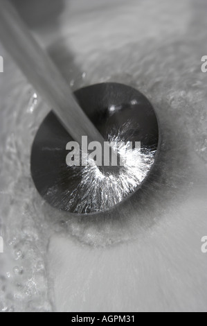 TAP WATER POURING DOWN PLUG HOLE IN WHITE BATHROOM SINK Stock Photo