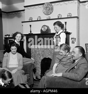 OLD VINTAGE BLACK AND WHITE FAMILY SNAPSHOT PHOTOGRAPH OF MOTHER FATHER AND FOUR CHILDREN RELAXING IN LIVING ROOM OF HOUSE 1950 Stock Photo