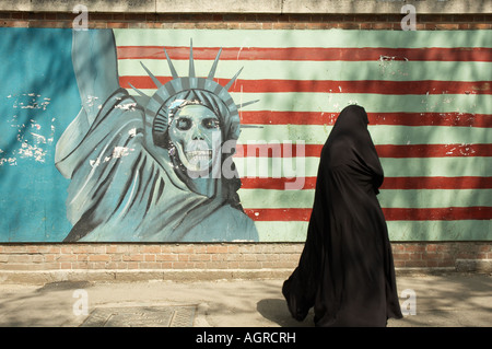 A woman wearing chador (Islamic Hijab) walking in front of a defaced statue of liberty and the USA flag on Outside walls of the Stock Photo