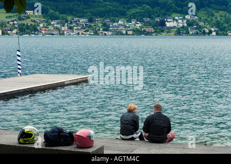 Man and woman in motorcycle gear sitting together on the shore of Traunsee Lake. Gmunden, Salzkammergut, Austria. Stock Photo
