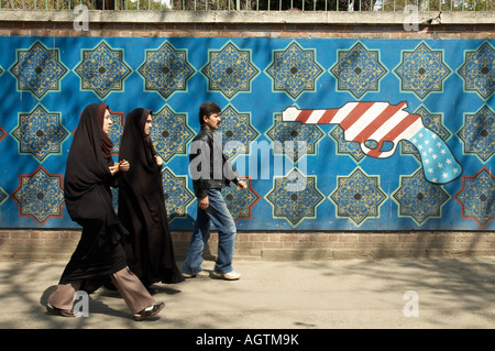 Two women in black chadors and a man walk past an anti-American pistol mural on the outside wall of the former US Embassy in Tehran, Iran. Stock Photo