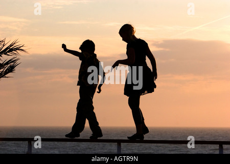 Silhouette of children walking on a railing at sunset by the sea Stock ...