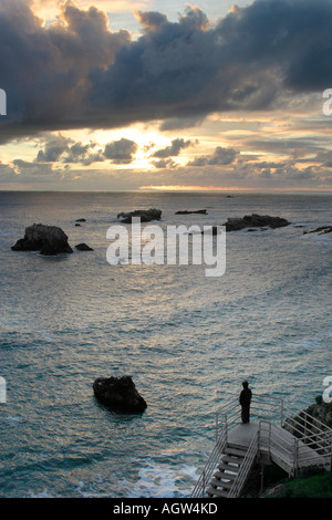 A person stands on a stairway that leads to a dramatic sunset over the ocean Stock Photo