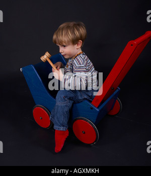 little boy in colourful woollen clothes sitting in wooden trailer Stock Photo