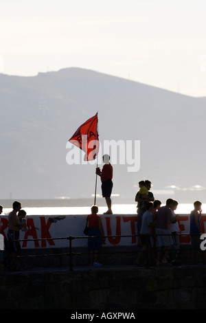 Man in silhouette holding red flag on sea wall during regatta Puerto Viejo de Algorta Basque Country Spain Stock Photo