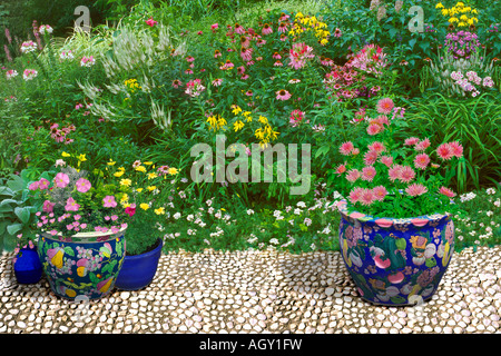 White cobblestone terrace with large Oriental ceramic pots with colors matching the wildflower garden of pink white and yellow Stock Photo