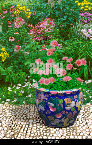 White cobblestone terrace with large Oriental ceramic pots  with colors matching the wildflower garden of pink white and yellow Stock Photo