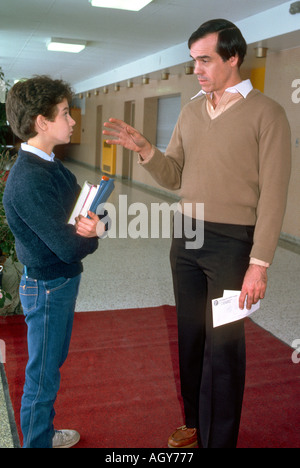 Male teacher disciplines middle school student between classes in school hallway Stock Photo