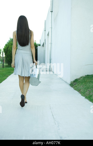 Woman carrying watering can, rear view, full length Stock Photo