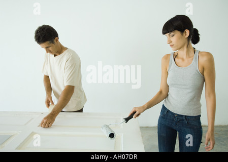 Woman painting door with paint roller, man protecting woodwork with masking tape Stock Photo
