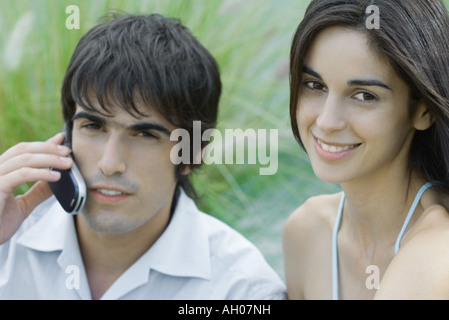Young couple, woman looking at camera, man using cell phone, head and shoulders, portrait Stock Photo